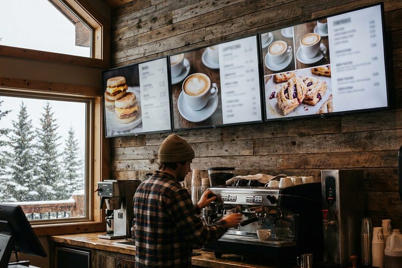 Digital menu boards with food photos above a coffee shop counter